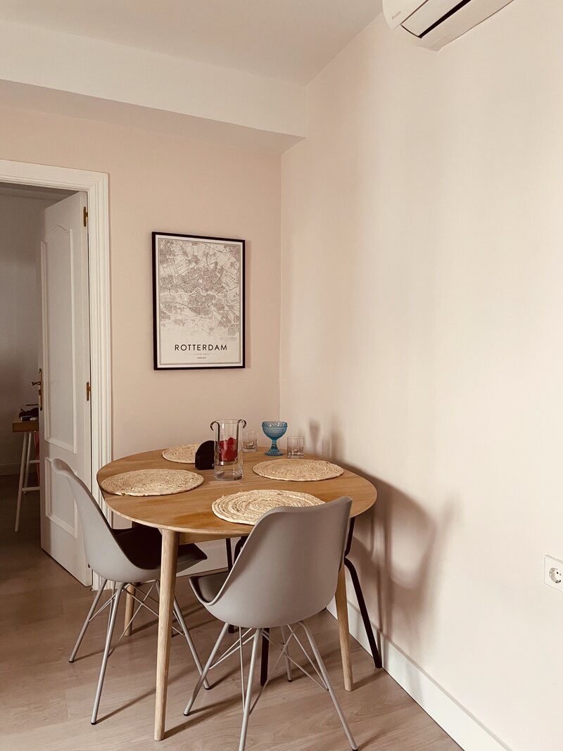 Comedor con mesa redonda de madera, sillas grises y lámina de Rotterdam enmarcada
